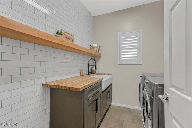 clothes washing area featuring cabinet space, light tile patterned floors, baseboards, washing machine and clothes dryer, and a sink