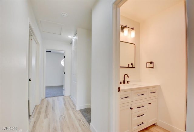 hall featuring baseboards, a sink, light wood-style flooring, and attic access