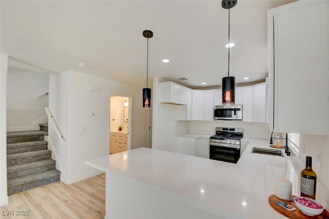 kitchen featuring light wood finished floors, light countertops, appliances with stainless steel finishes, a sink, and a peninsula