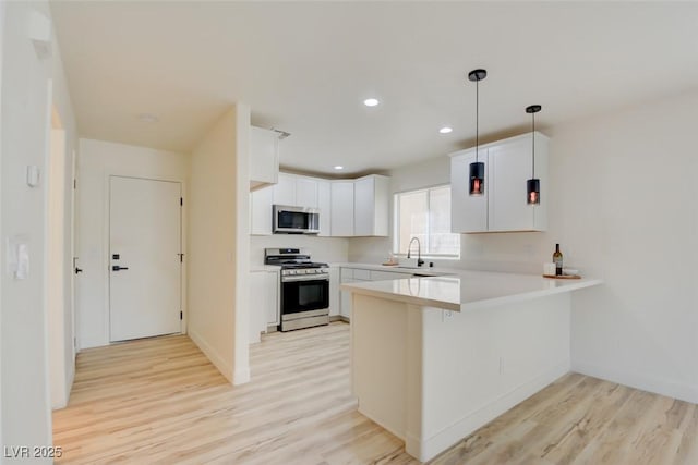 kitchen featuring stainless steel appliances, white cabinetry, a sink, light wood-type flooring, and a peninsula