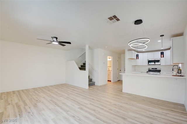 kitchen with range, light wood-style flooring, stainless steel microwave, open floor plan, and light countertops