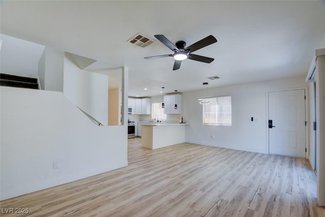 unfurnished living room featuring light wood-type flooring, a sink, visible vents, and a ceiling fan