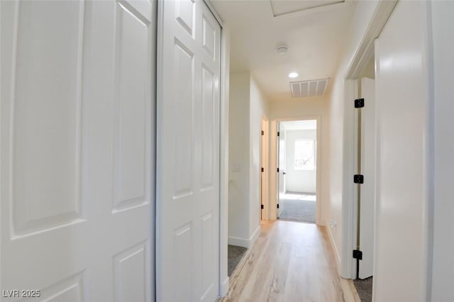 hall with baseboards, visible vents, and light wood finished floors