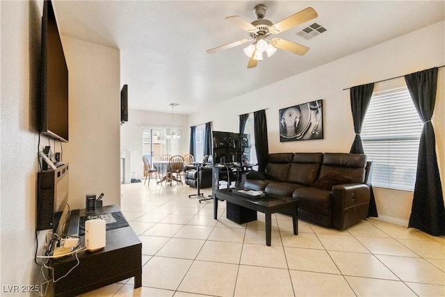 living area featuring ceiling fan with notable chandelier, visible vents, baseboards, and light tile patterned floors