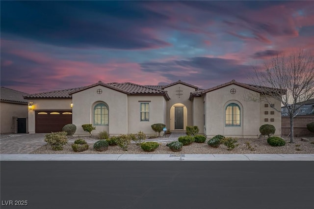 mediterranean / spanish-style home with a tiled roof, decorative driveway, an attached garage, and stucco siding