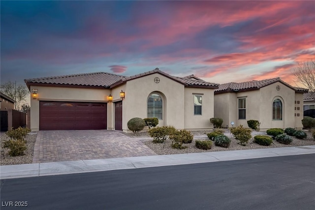 mediterranean / spanish-style home with a garage, decorative driveway, and stucco siding