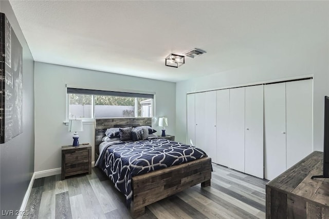 bedroom with a closet, visible vents, baseboards, and wood finished floors