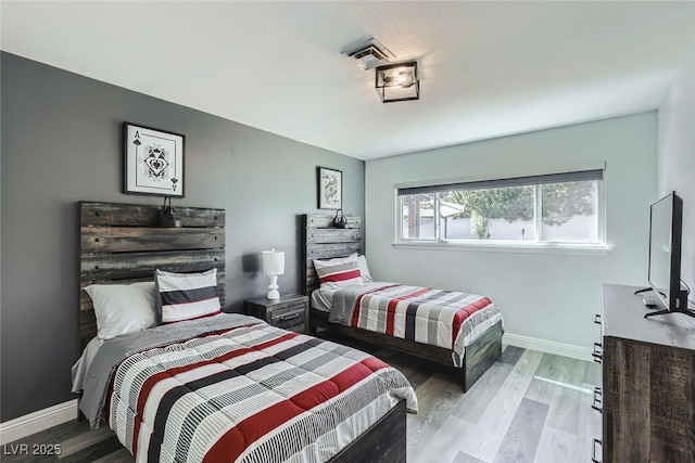 bedroom with wood finished floors, visible vents, and baseboards