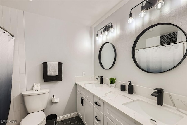 bathroom with baseboards, a sink, toilet, and double vanity