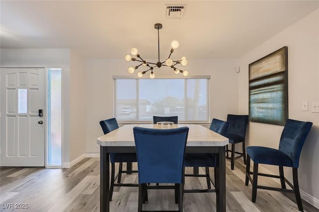 dining area featuring light wood finished floors, baseboards, visible vents, and a chandelier