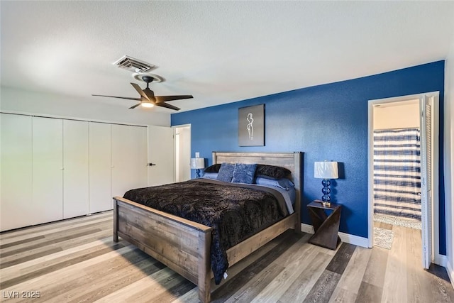 bedroom with baseboards, visible vents, a ceiling fan, wood finished floors, and a closet