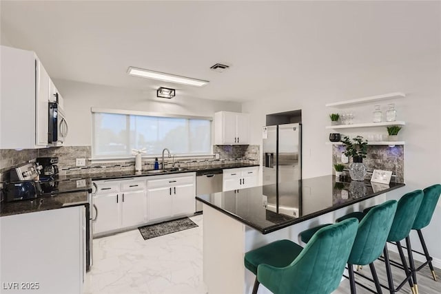 kitchen with a peninsula, marble finish floor, a sink, stainless steel appliances, and backsplash