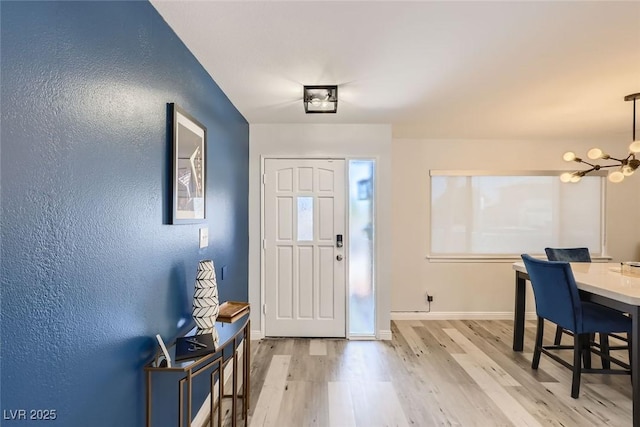 entrance foyer with light wood-type flooring, baseboards, and a notable chandelier