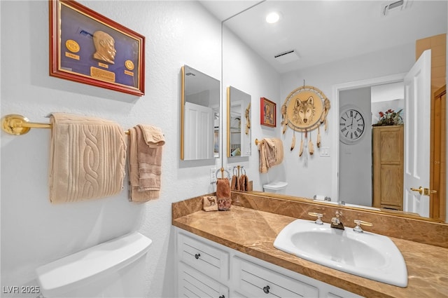 bathroom with toilet, visible vents, and vanity