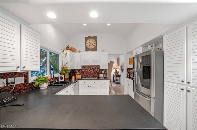 kitchen with decorative backsplash, dark countertops, lofted ceiling, stainless steel appliances, and a sink