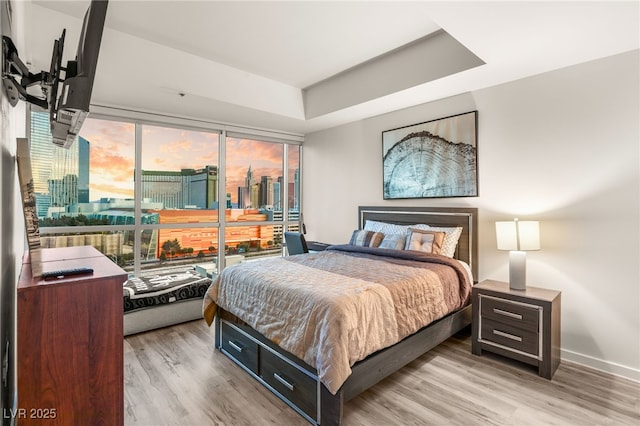 bedroom with light wood-type flooring, a raised ceiling, and baseboards