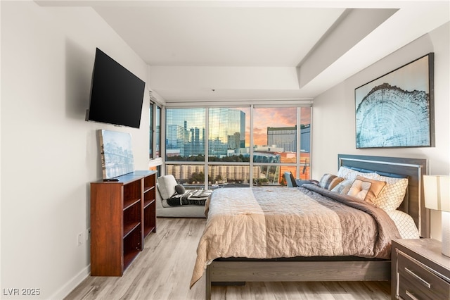 bedroom featuring light wood-style floors, floor to ceiling windows, and baseboards