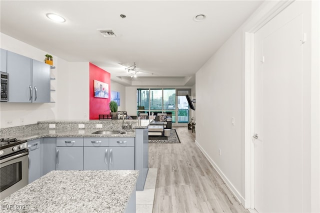 kitchen with visible vents, a peninsula, stainless steel gas range, open shelves, and a sink