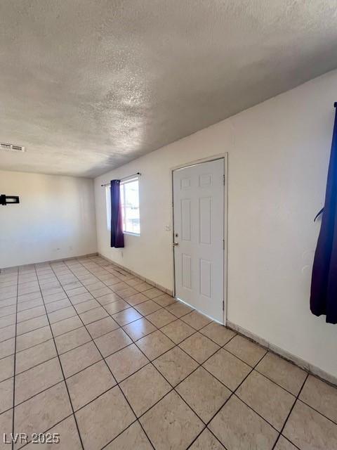 interior space featuring visible vents, a textured ceiling, baseboards, and light tile patterned floors