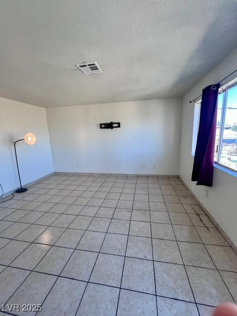 empty room featuring visible vents, a textured ceiling, and light tile patterned flooring