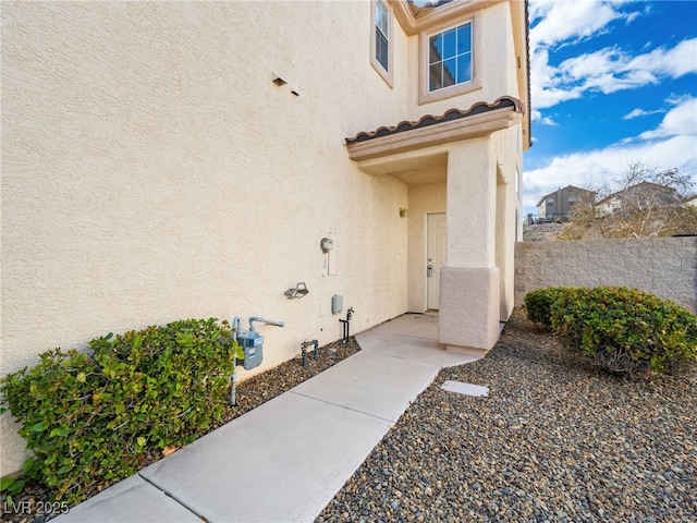 property entrance featuring a tiled roof, fence, and stucco siding