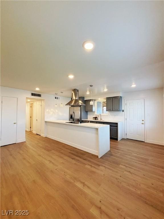 kitchen featuring light wood finished floors, light countertops, visible vents, a peninsula, and exhaust hood