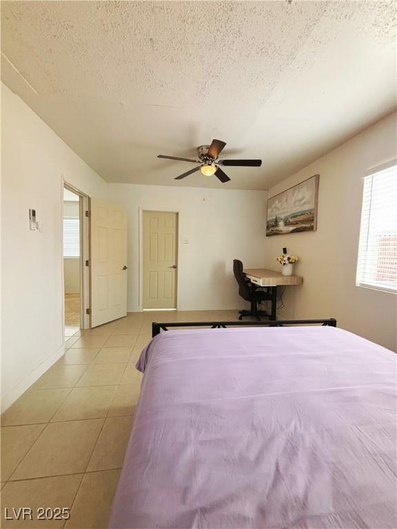 unfurnished bedroom with a textured ceiling, light tile patterned flooring, a ceiling fan, and baseboards