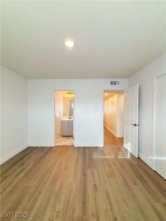 empty room with light wood finished floors, visible vents, and baseboards