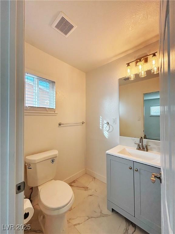 half bath with toilet, vanity, visible vents, baseboards, and marble finish floor