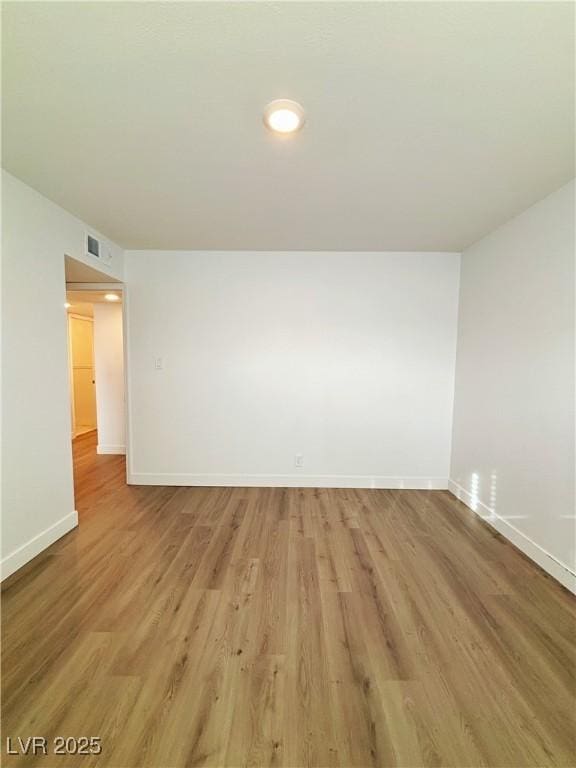 spare room with light wood-type flooring, visible vents, and baseboards