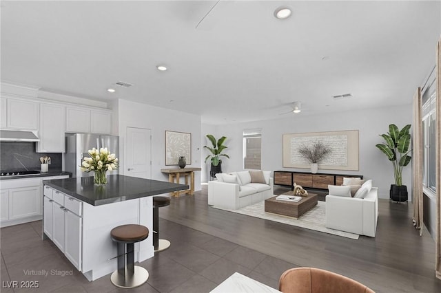 kitchen featuring range hood, black electric stovetop, visible vents, freestanding refrigerator, and open floor plan