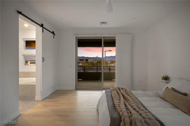 bedroom featuring a barn door, visible vents, connected bathroom, wood finished floors, and access to outside