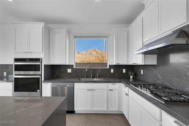 kitchen with appliances with stainless steel finishes, white cabinets, a sink, light tile patterned flooring, and under cabinet range hood