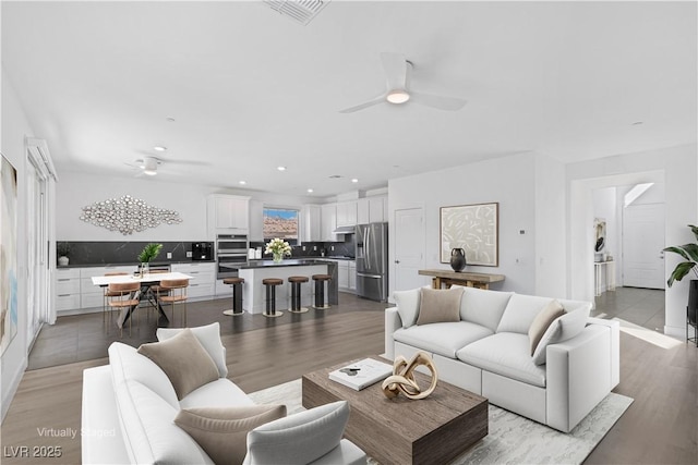 living area featuring ceiling fan, visible vents, and wood finished floors