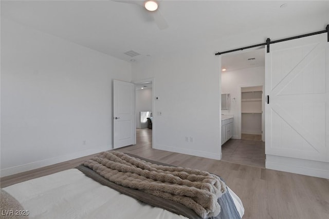 bedroom with a barn door, visible vents, light wood-style flooring, and baseboards