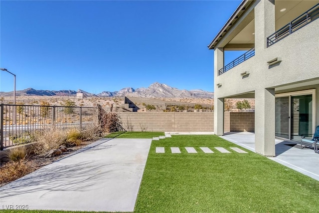 view of yard featuring a patio area, a mountain view, a fenced backyard, and a balcony