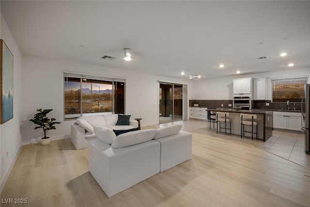 living room with light wood-type flooring, visible vents, baseboards, and recessed lighting