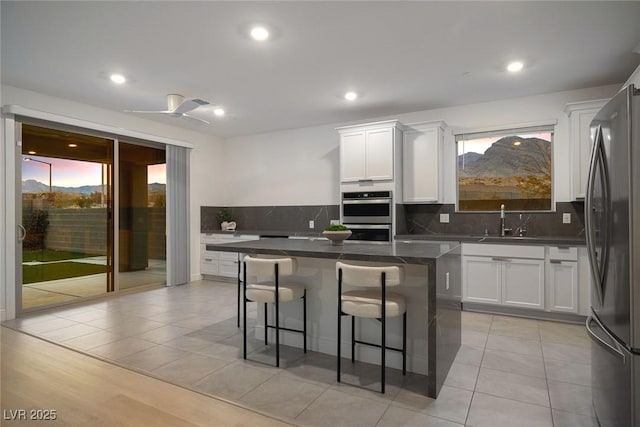 kitchen featuring tasteful backsplash, white cabinets, dark countertops, appliances with stainless steel finishes, and a kitchen breakfast bar