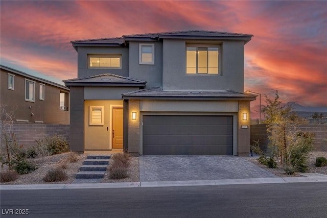 view of front of house with a garage, fence, decorative driveway, and stucco siding