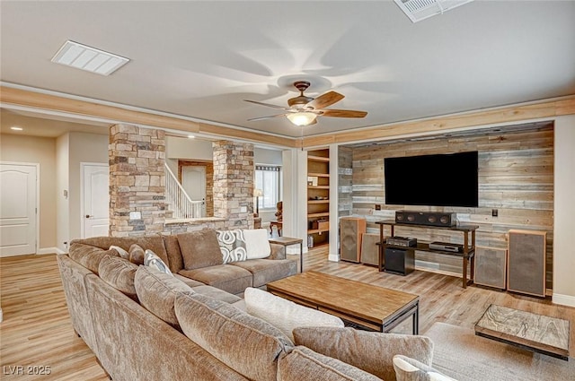 living area featuring built in features, visible vents, a ceiling fan, light wood-style floors, and ornate columns