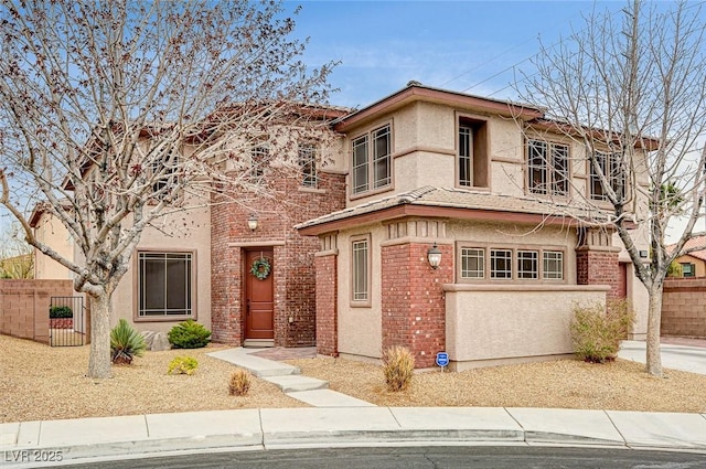 view of front of house featuring brick siding, fence, and stucco siding