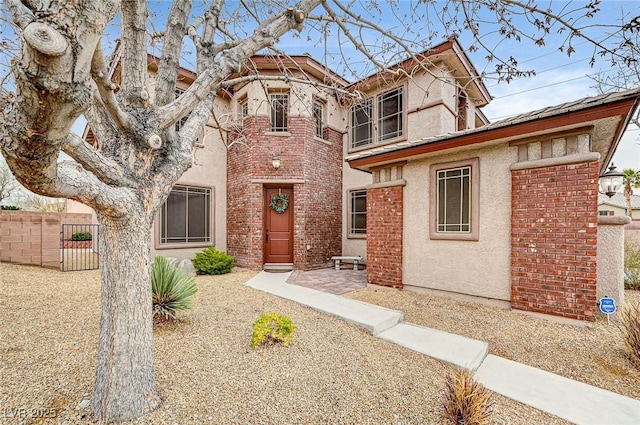 view of front of home featuring stucco siding, a gate, fence, and brick siding