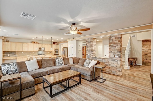 living area featuring light wood-style floors, decorative columns, visible vents, and a ceiling fan