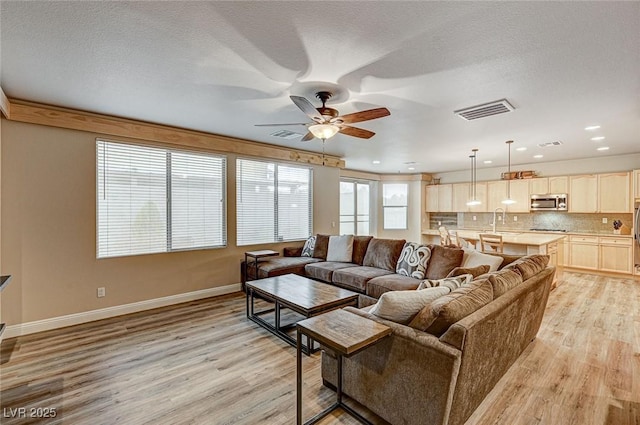 living area with baseboards, visible vents, a textured ceiling, and light wood finished floors