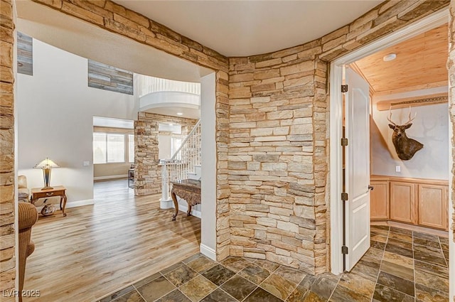 hallway with arched walkways, a wainscoted wall, stone tile floors, and stairs