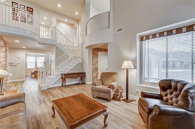 living area featuring wood finished floors, visible vents, a towering ceiling, and stairs