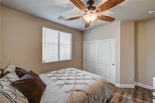 bedroom featuring ceiling fan, wood finished floors, visible vents, baseboards, and a closet