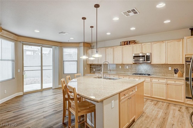 kitchen with light brown cabinetry, stainless steel microwave, a sink, and visible vents