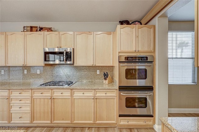 kitchen with light brown cabinets, light stone counters, stainless steel appliances, and backsplash