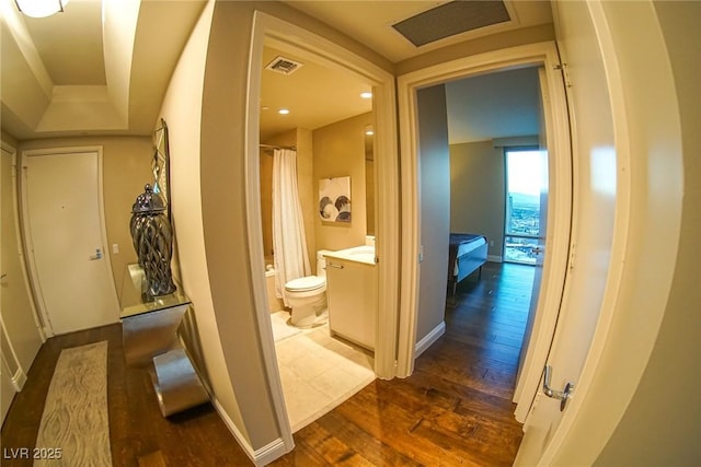 hall with dark wood-type flooring, visible vents, and baseboards